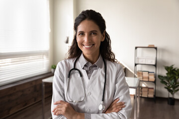 Happy female GP doctor in white coat with stethoscope looking at camera, smiling. Head shot...