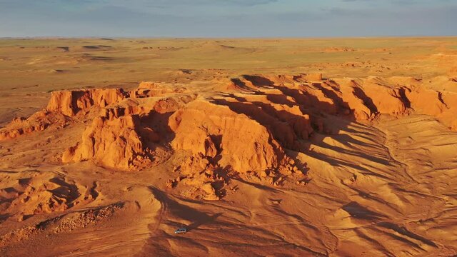 Aerial around view of the Bayanzag flaming cliffs and car at sunset in Mongolia, found in the Gobi Desert, 4k