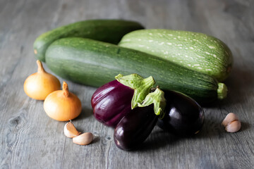 Eggplants, zucchini, onions and garlic on a gray wooden table.