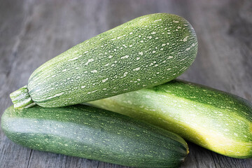 Green whole zucchini on a gray wooden table. Close-up.