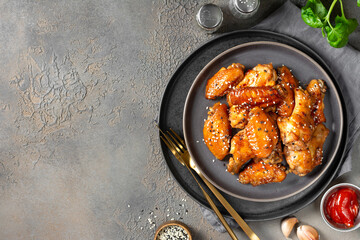 Homemade baked or fried chicken wings in barbecue sauce in a plate on the cooking table top view with copyspace	
