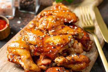 Homemade baked or fried chicken wings in barbecue sauce on a serving board on a cooking table closeup	