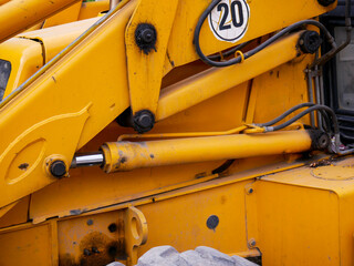 Hydraulic connections on a yellow excavator near roadside in a small city.