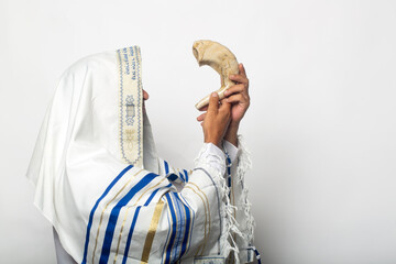 Jewish man in tallit blowing the Shofar of Rosh Hashanah (New Year). Religious symbol. Blowing the shofar for the Feast of Trumpets, jew in a traditional tallit prayer shawl blowing the ram's horn - obrazy, fototapety, plakaty
