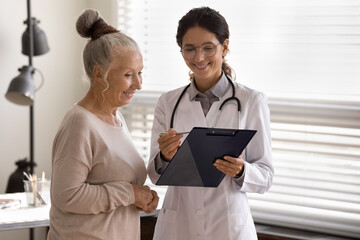 Happy smile GP therapist showing pad to mature 70s female patient, explaining prescription, medical...