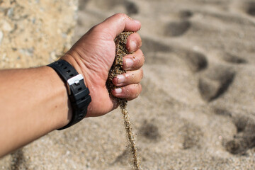 The passage of time - concept. The hand of a man from whom the sand leaks. The scene on the beach.