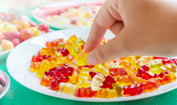 Hand takes colorful gummy bears candies of the plate. Close-up. Jelly treats for children and adults.