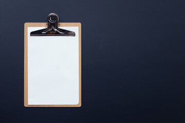 Wooden clipboard with blank white paper on dark background.