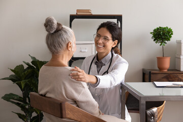 Happy satisfied GP doctor telling good news to elder patient, congratulating on optimistic medical...