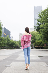 Fototapeta na wymiar Portrait of young asian woman from behind wearing stylish casual clothing and walking outdoor in city. Happy stylish woman enjoys life