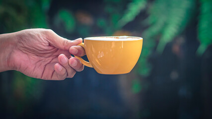 Close-up isolated hand holding yellow mug on black background. hand hold simple yellow cup. Perfect for both tea and coffee.