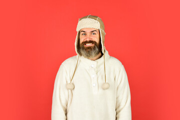 Bearded man wear hat with ear flaps red background. Soft furry accessory. Caring fur garments. Bearded funny hipster. Winter fashion concept. Warm hat for cold weather. Sheep fur. Perfect accessory