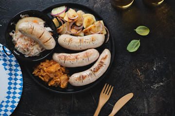 Above view of pan fried munich sausages with sauerkraut, stewed cabbage and potato salad, horizontal shot on a dark brown stone background
