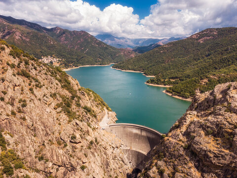 Aerial view of the dam wall at Lac de Tolla and the village of Tolla in Corsica surrounded by pine forest with mountains in the distance