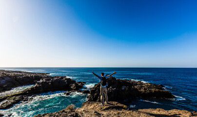 Fototapeta premium young bright attractive man standing on the ocean and controlling the situation on the beach. Ocean waves and blue sky background
