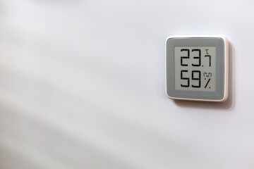 Indoor gray plastic digital thermometer on white wall showing temperature, humidity level, smiling...