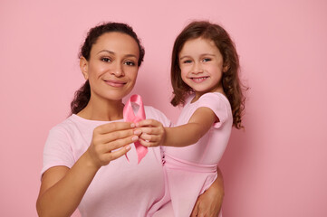 Two generations of women, mom and daughter hugging each other, holding pink ribbon, Breast Cancer awareness day symbol, showing support and solidarity to patients and cancer survivors. Women's health