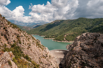 The dam wall at Lac de Tolla in Corsica surrounded by rocky cliffs and pine forest with mountains in the distance