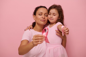 Adorable mixed-race woman mother hugs a little girl in pink outfits and displays a pink satin...
