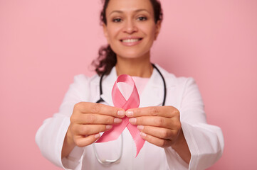 Soft focus on Breast Cancer Awareness Pink Ribbon, in hands of blurred mixed race female doctor in...