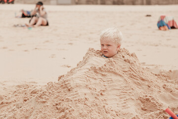 Little boy buried in pile of sand on the beach