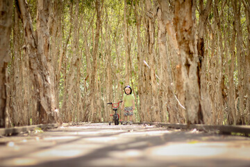 Boy riding bike along walkway surrounded by tall paperbark trees