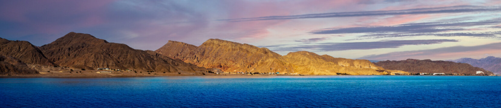 Coast of the Red Sea in the Gulf of Aqaba on the border of Egypt and Israel, Taba region, Sinai. Panoramic landscape with mountain ranges and beautiful cloudy sky at sunset.