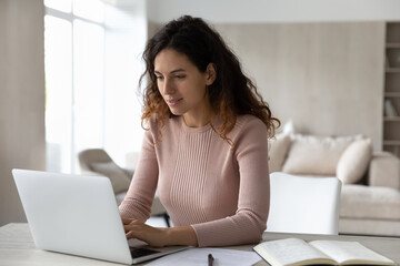 Happy attractive young woman freelancer working on computer at home, preparing electronic report, editing documents, creating online project, analyzing sales statistics data or studying distantly.