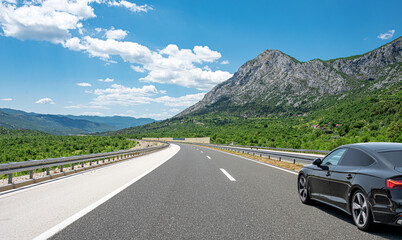 Black car on a scenic road. Car on the road surrounded by a magnificent natural landscape.