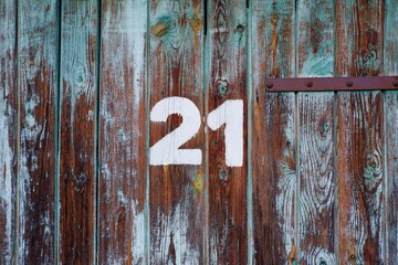 White colour number twenty-one on an old abandoned brown and blue colour wooden gate 