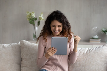 Overjoyed emotional young latina woman looking at digital tablet screen, celebrating online lottery...