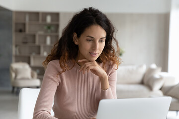 Smiling beautiful young hispanic ethnic woman looking at laptop screen, enjoying working on online...