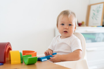 Blond adorable blue-eyed caucasian toddler playing and learning with plastic constructor. Concept of child motor development, education and leisure activity at kindergarten. Horizontal, copy space