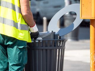 operator with reflective life jacket and rubber gloves replaces the bag in a waste bin