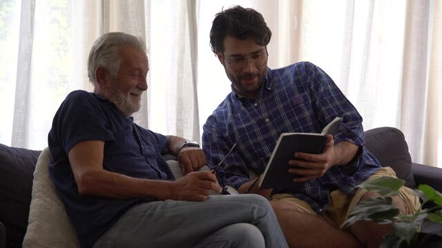 happy Senior Father and adult son reading book or diary  remembering of the Past together on sofa in the room at home . two generations family good memories by notebook