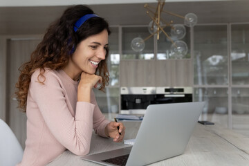 Smiling confident young latina woman in headphones looking at laptop screen, watching educational...