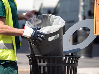street sweeper with reflective life jacket and rubber gloves replaces the bag in a waste basket