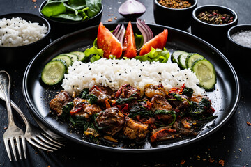 Roast pork  with jasmine rice and vegetables served on black plate on wooden table