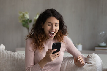 Overjoyed emotional young latin woman looking at smartphone screen, celebrating getting amazing news, feeling excited of online lottery auction betting giveaway win, internet success concept.