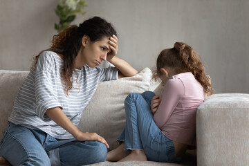 Depressed young latin mother feeling guilty looking at stressed little child daughter, having...