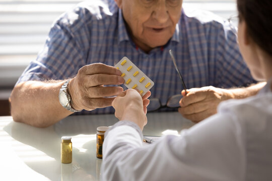 Female GP doctor giving pills to older male patient at appointment. Practitioner prescribing medicine to senior 80s man, drugs for mental health, geriatric disease prevention, dementia treatment