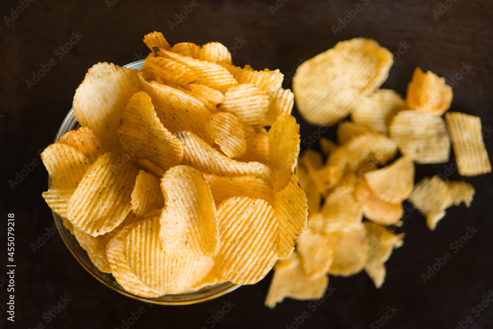 Poster Crispy potato chips in a plate on metallic black grunge background