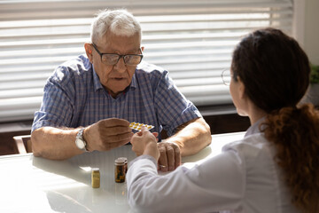 Confused older 80s male patient taking pills from GP doctor for mental health, consulting about...