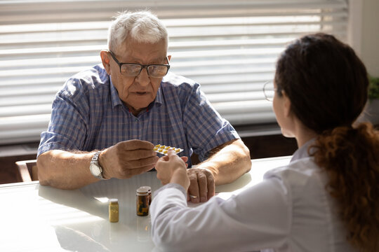 Confused older 80s male patient taking pills from GP doctor for mental health, consulting about dementia therapy. Female practitioner prescribing drugs, medications to senior mature man at appointment