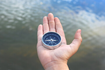 Old classic navigation compass in hand on natural background as symbol of tourism with compass,...