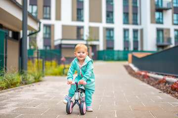 Cute little toddler girl in blue overalls riding on run balance bike. Happy healthy lovely baby...