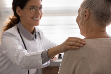 Happy general practitioner telling good optimistic news to older patient, touching shoulder of...