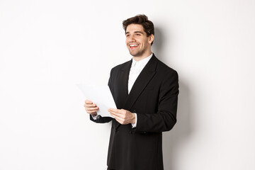 Obraz na płótnie Canvas Image of handsome businessman in suit, holding documents and smiling, standing against white background