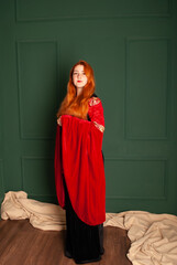 Obraz premium Charming cute girl with red hair shows a beautiful dress of a vampire witch for halloween concept of fear and horror