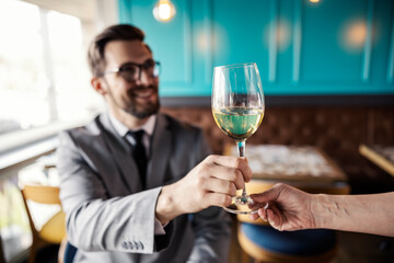 Crystal glass full of white wine. A male guest in a business suit sits at a table in a restaurant and takes a glass of cold alcohol. Focus the photos on the hands holding a glass full of wine